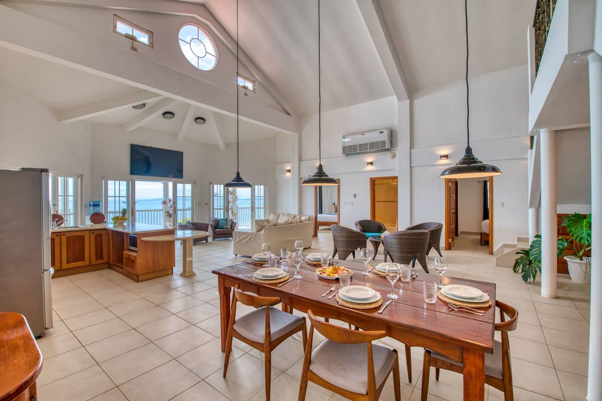 A spacious dining area with a high ceiling, large windows, and a view of the outdoors.