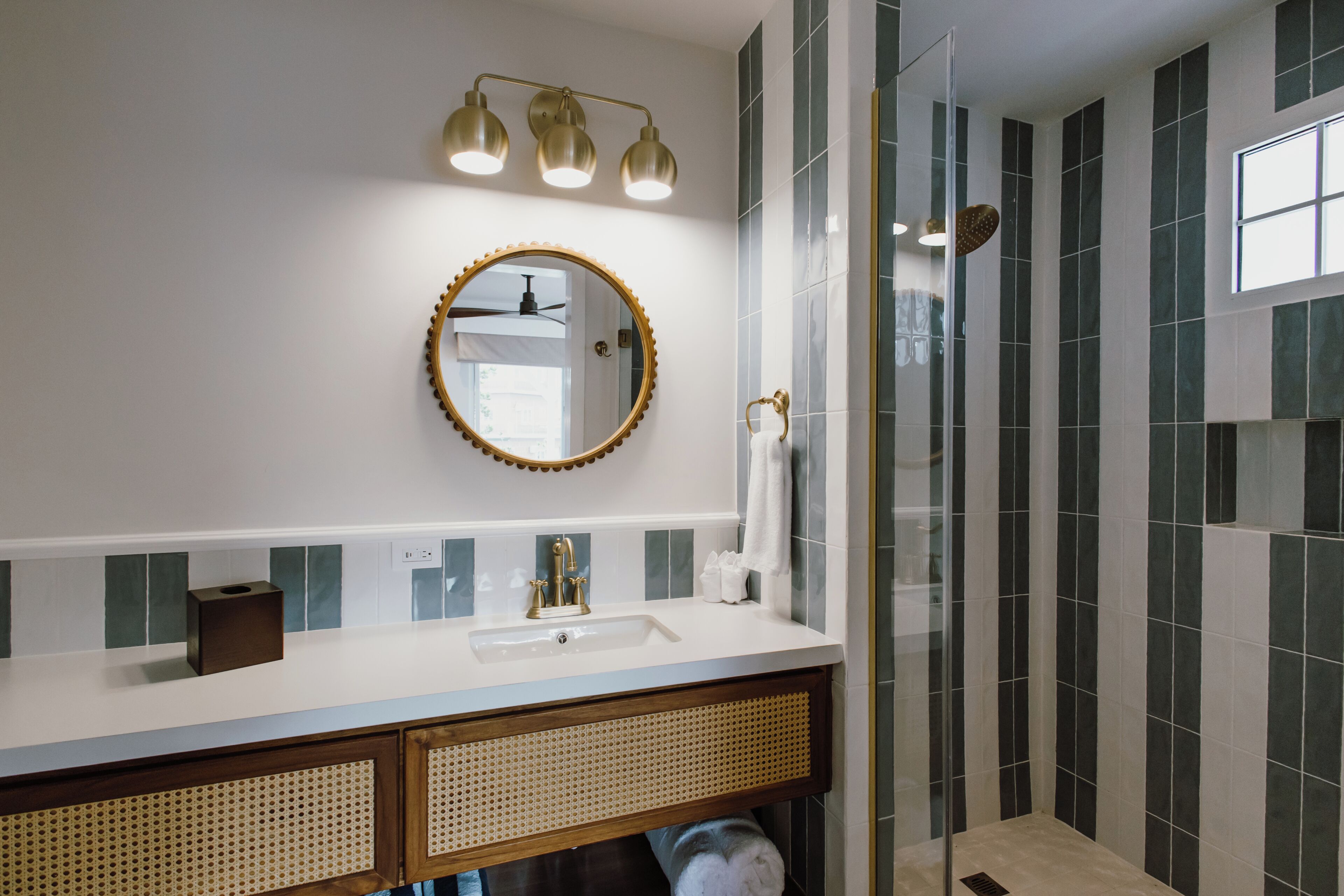 A bathroom with a white sink, a round mirror with a gold frame, and a shower area with dark tiles.