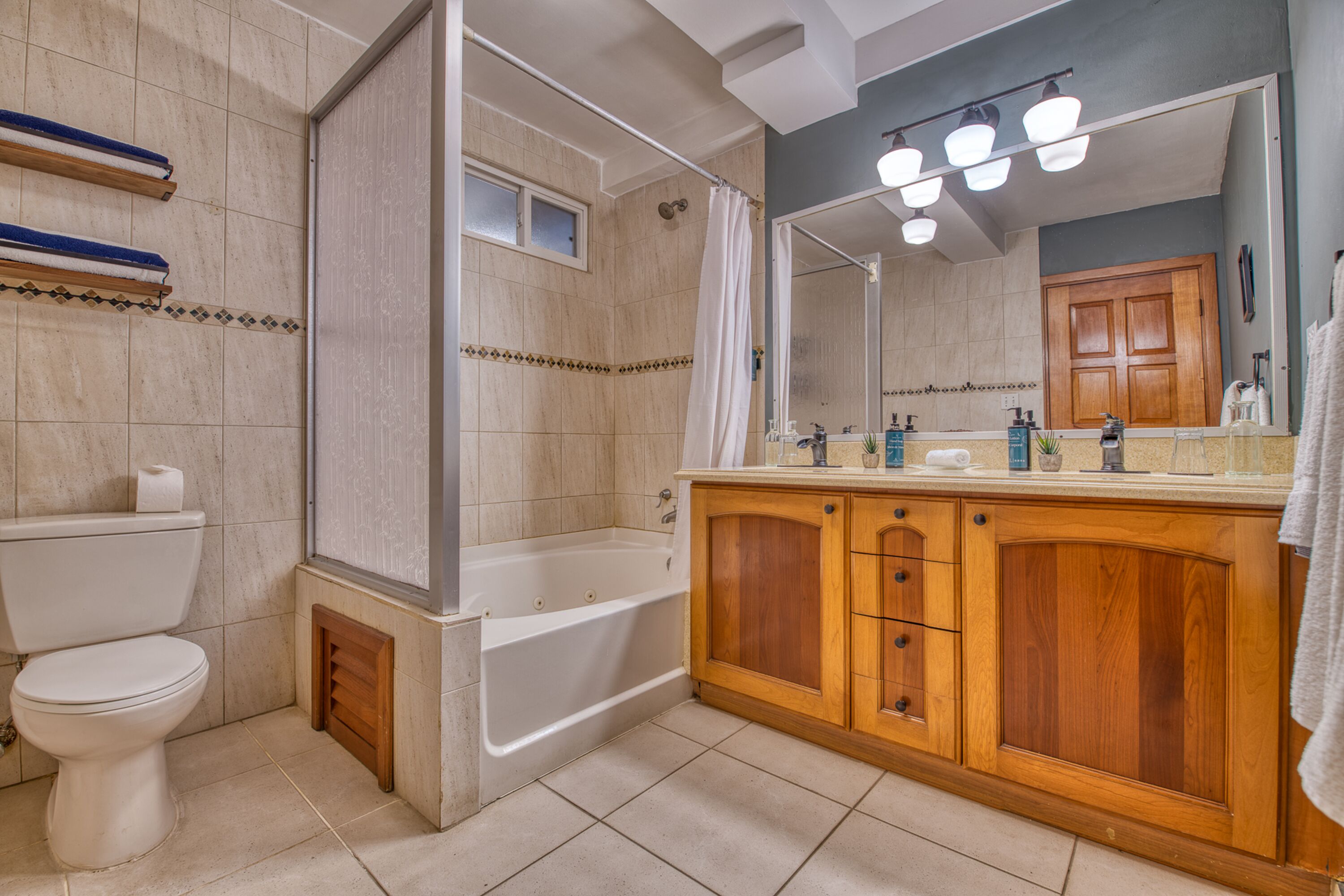 Une salle de bain comprenant des toilettes, une baignoire, un meuble-lavabo en bois et un grand miroir.