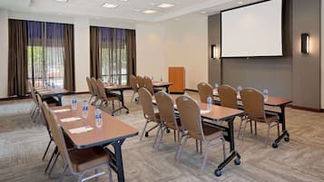 A conference room with tables, chairs, a projector screen, and water bottles.