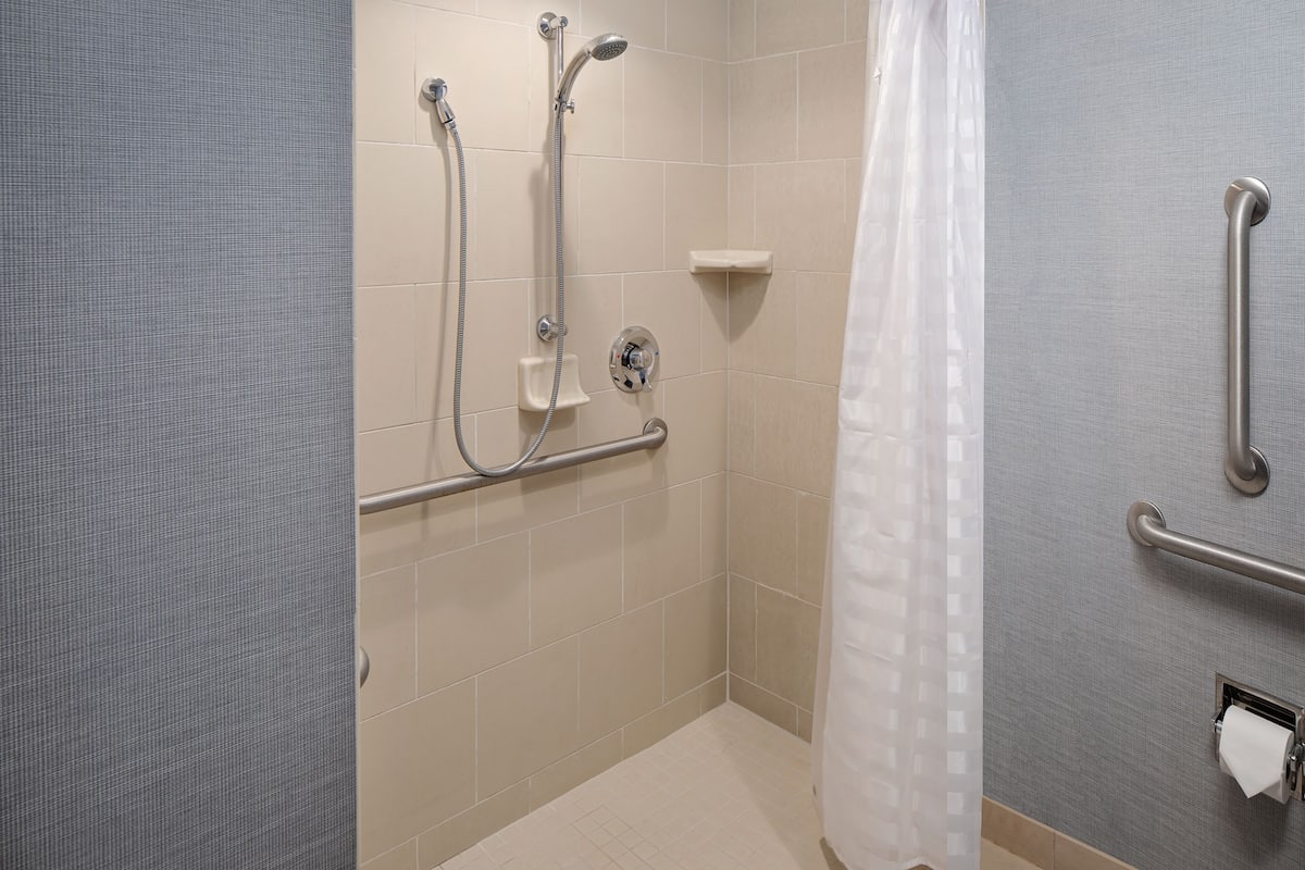 A bathroom with a shower, grab bars, and a toilet paper holder.