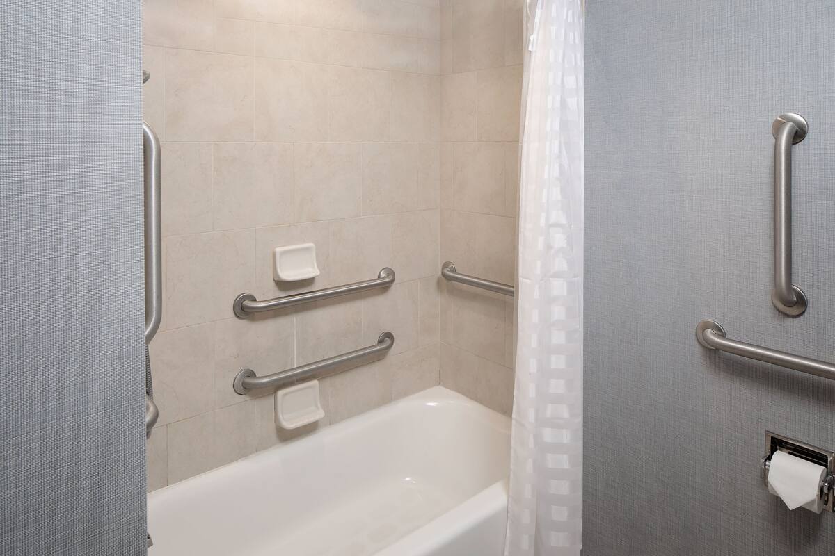 A bathroom with a white bathtub, grab bars, and a towel dispenser.