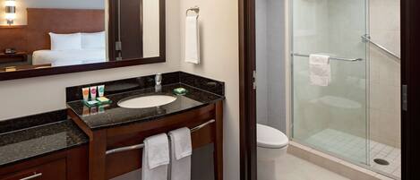 A modern bathroom with a glass-enclosed shower, a sink with a marble countertop, and a large mirror above the vanity.