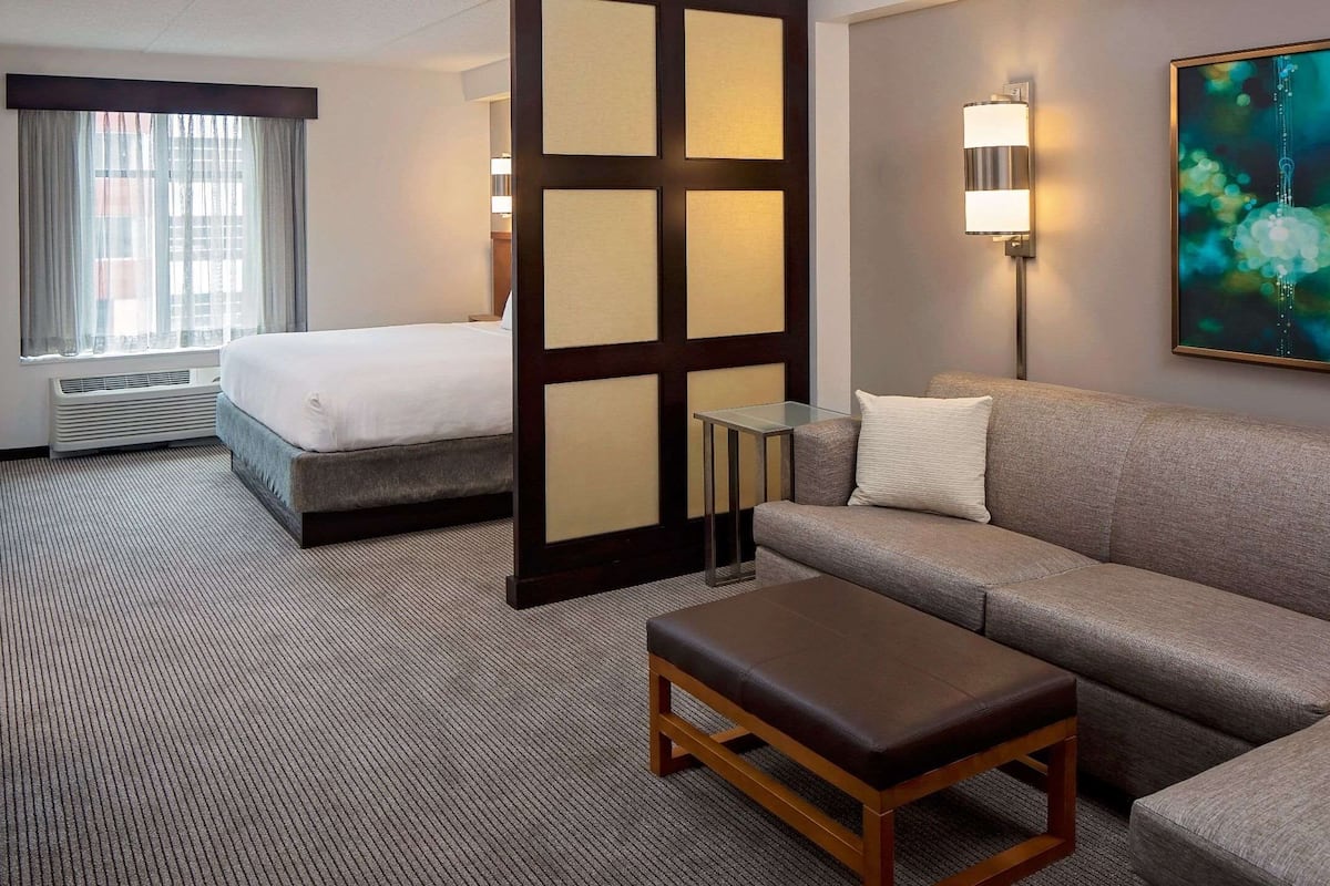 A hotel room with a bed, a sofa, a TV, a desk, and a painting on the wall.