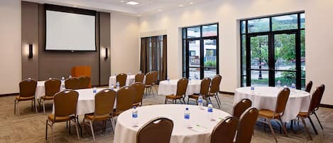 A conference room with multiple tables and chairs, large windows, and a projection screen.