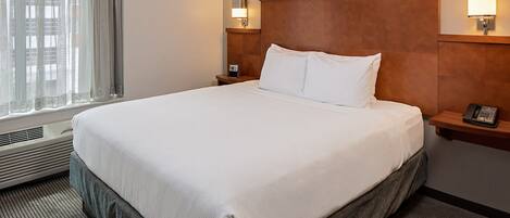 Habitación de hotel con una cama grande, dos mesitas de noche y un ventanal con cortinas.