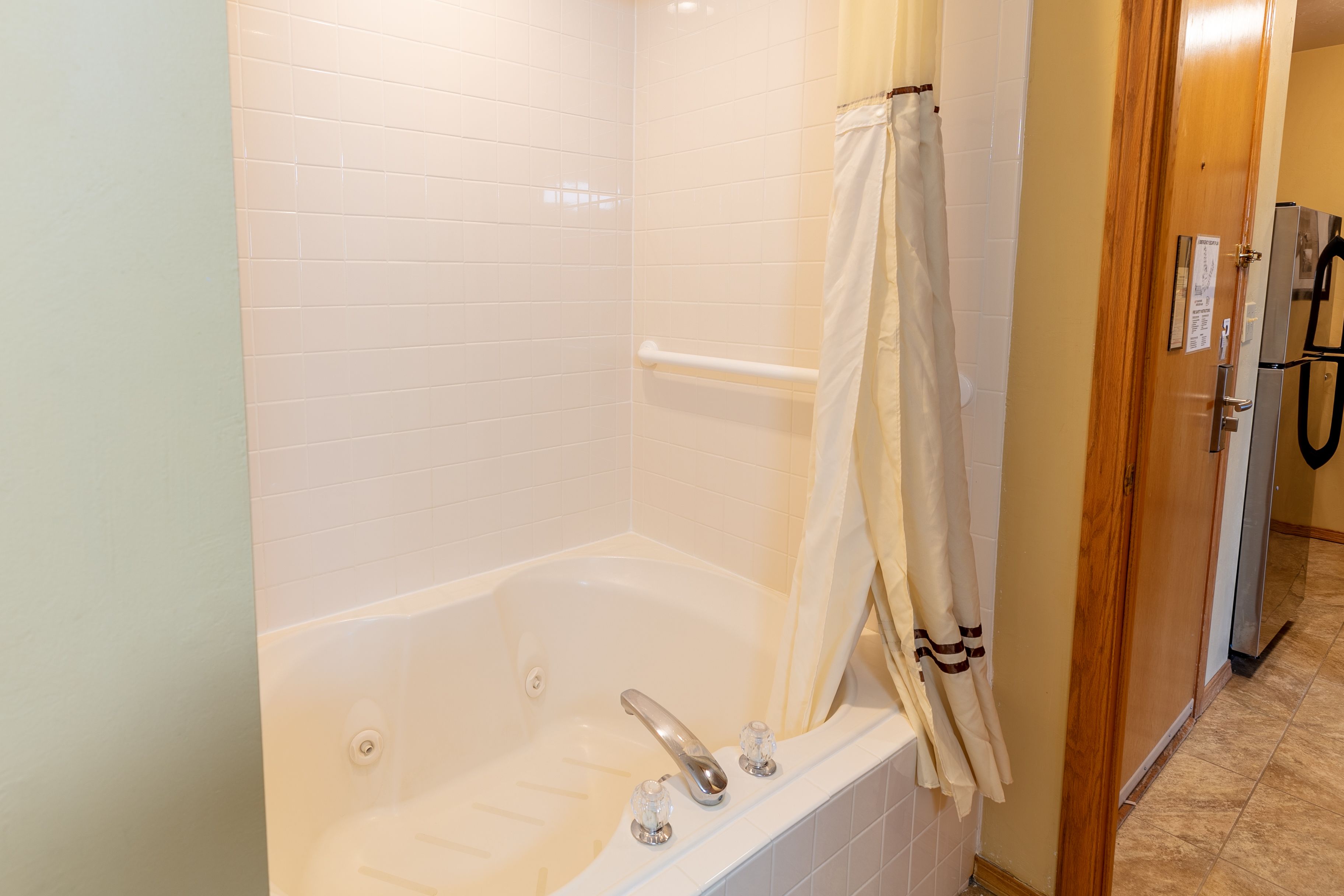 A bathroom with a bathtub, a shower curtain, and a door leading to a hallway.