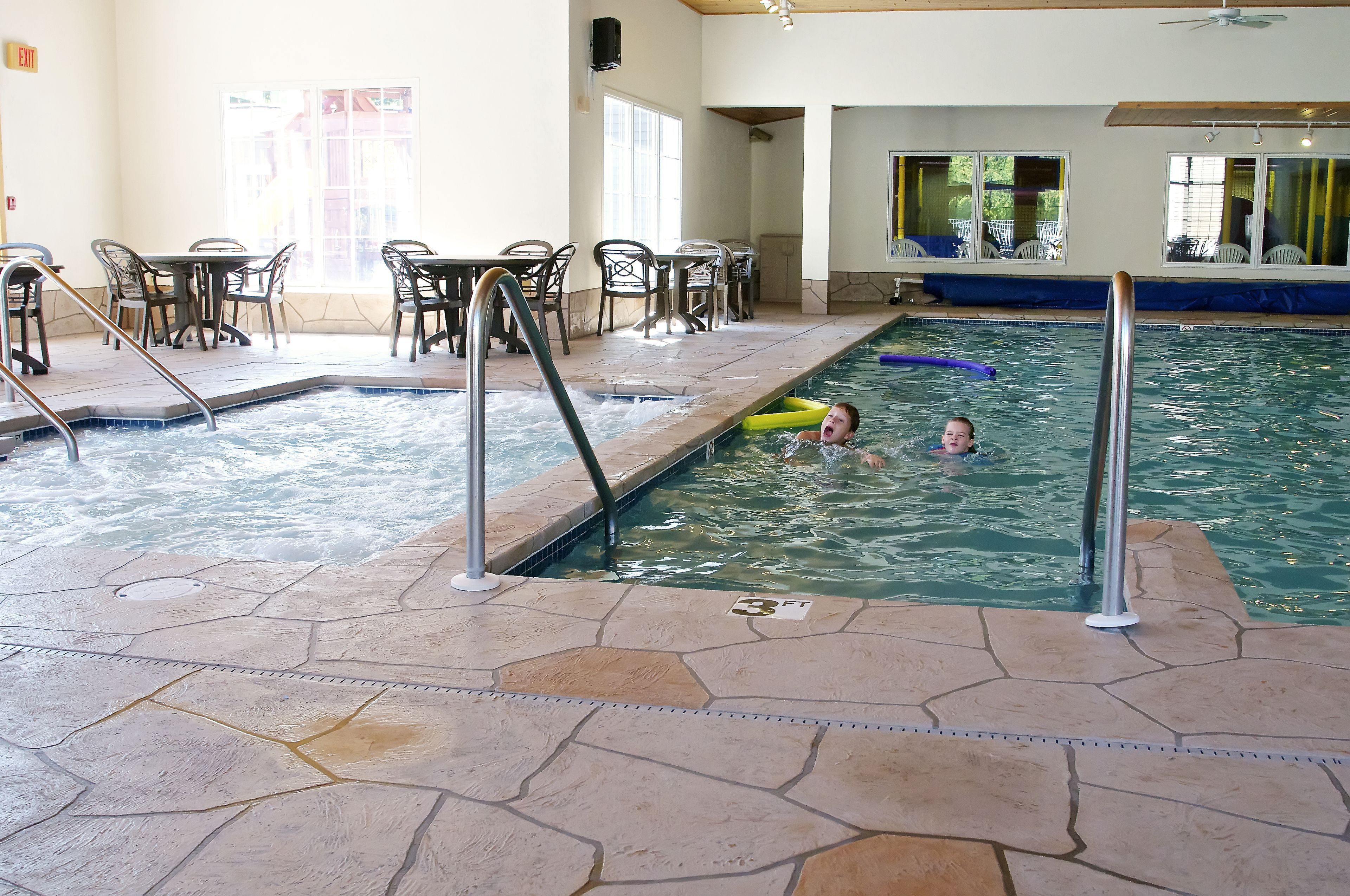 Une piscine intérieure avec un sol carrelé, un poste de surveillance pour les maîtres-nageurs et une table de billard avec des chaises.