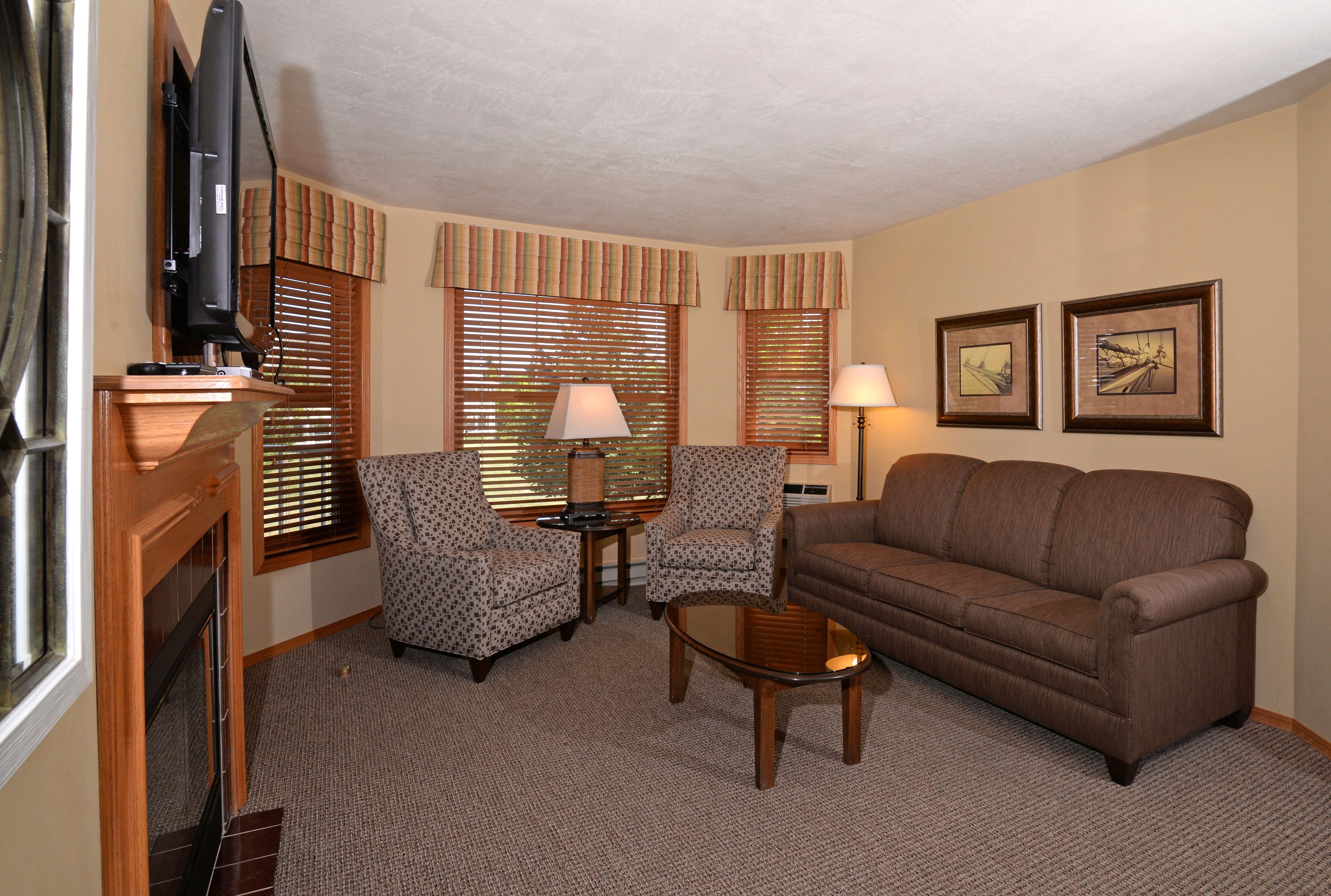 A living room with a brown sofa, two patterned armchairs, a coffee table, a television, and a fireplace.