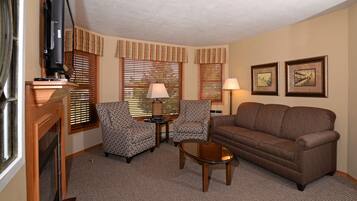 A living room with a brown sofa, two patterned armchairs, a coffee table, a television, and a fireplace.