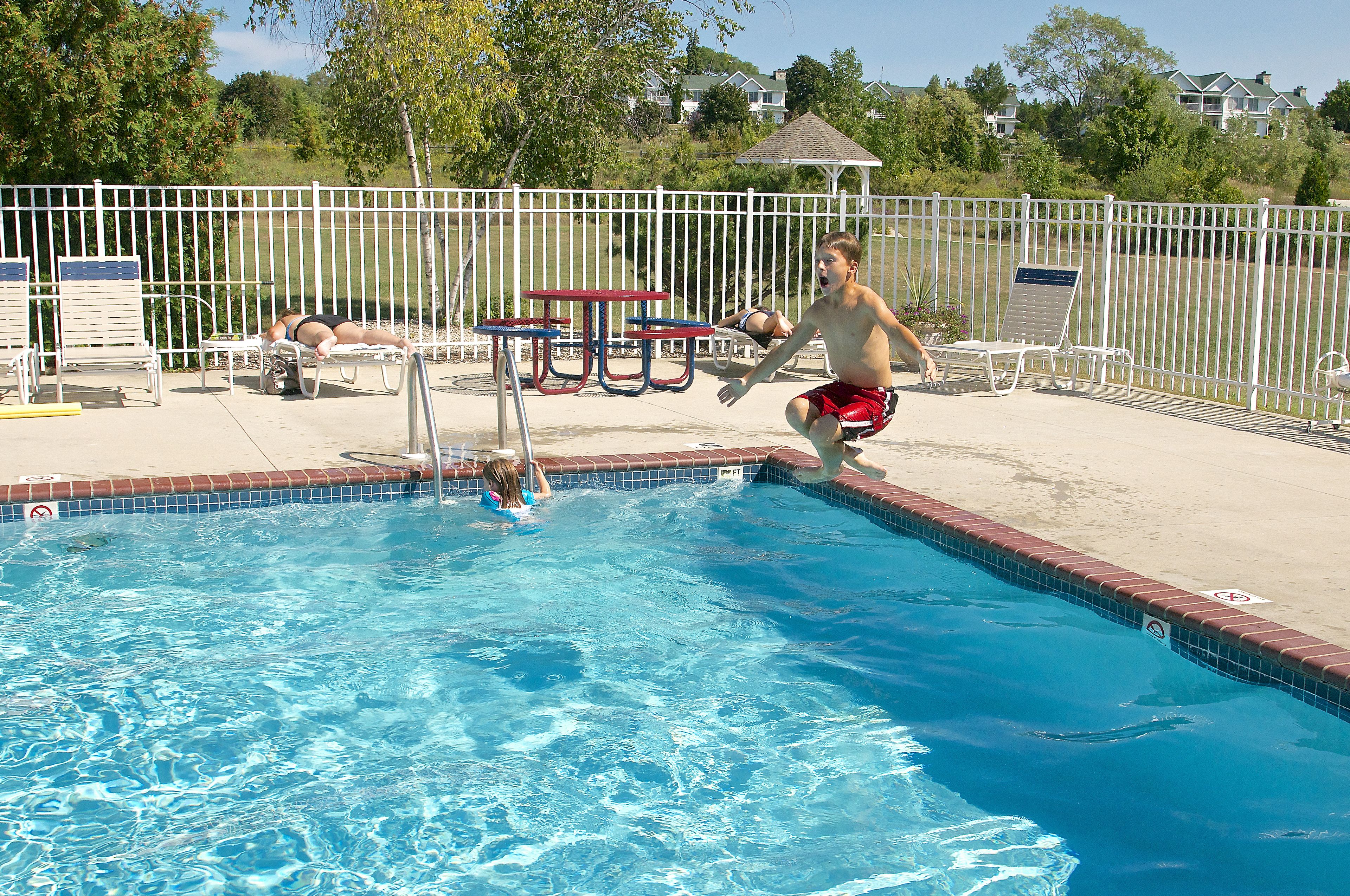 Piscina con valla blanca, sillas de descanso y mesa de picnic.