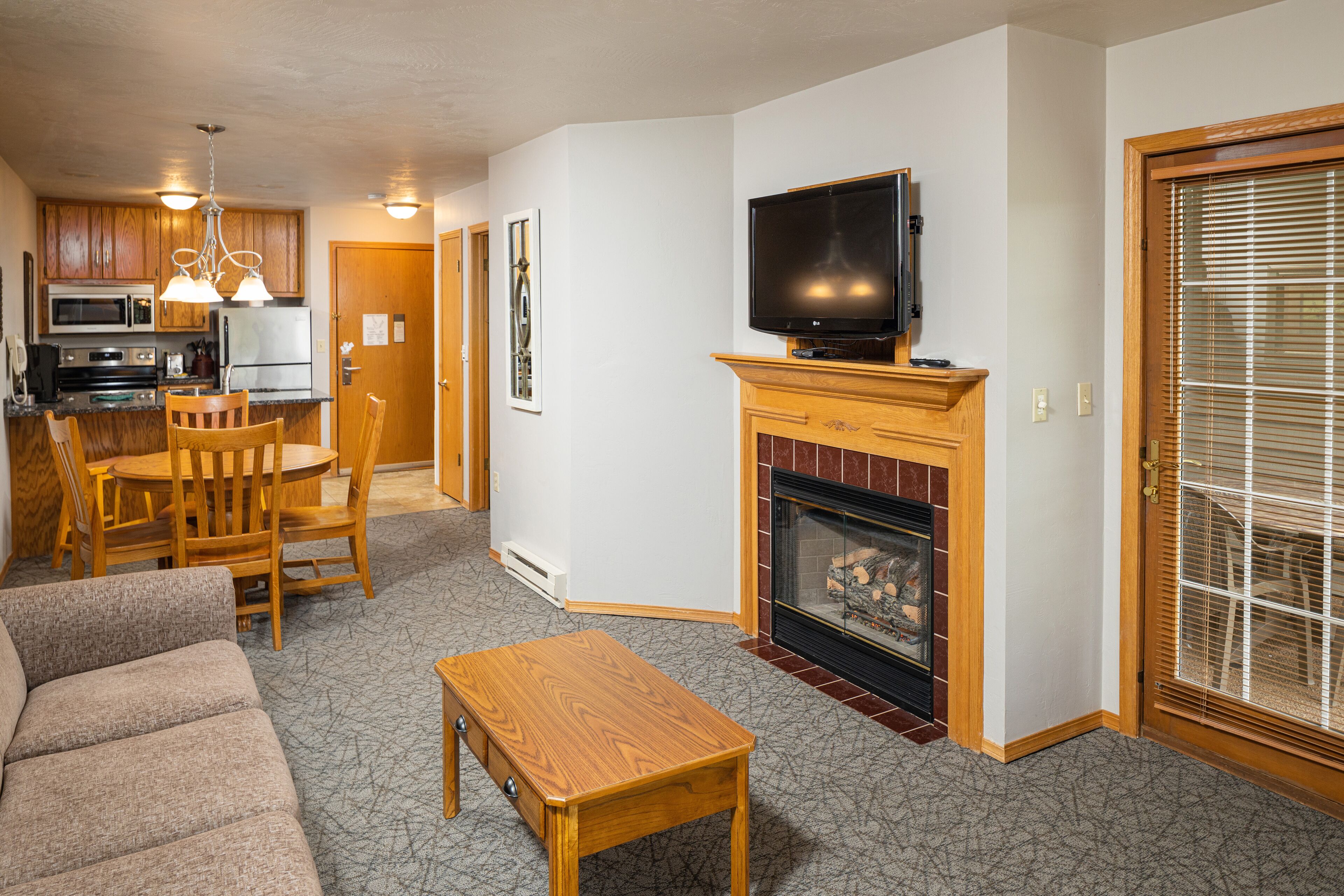 Una sala de estar con chimenea, televisor y comedor con mobiliario de madera.