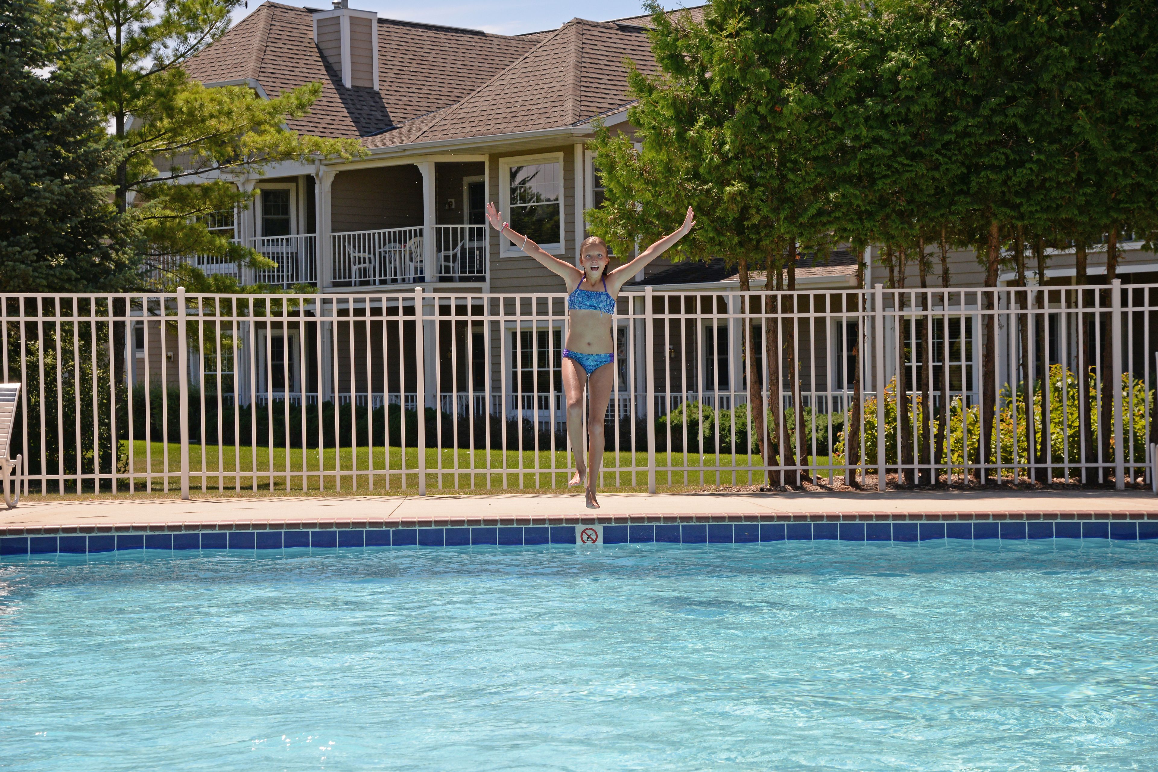 A swimming pool with a white fence and a house in the background.