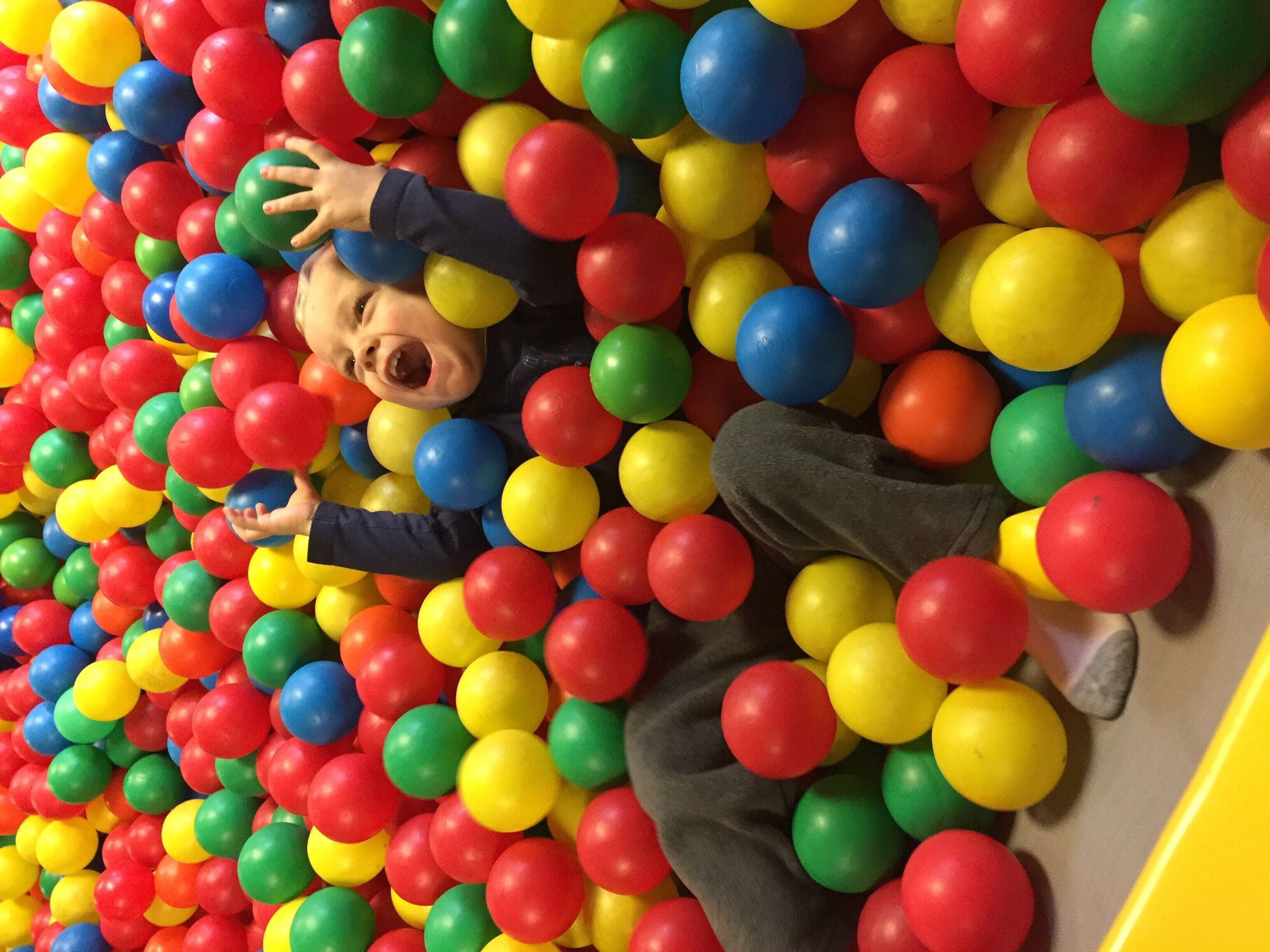 A child lying in a ball pit filled with multicolored balls.