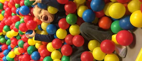 A child lying in a ball pit filled with multicolored balls.