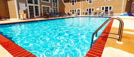 A swimming pool with a red border, lounge chairs, and a building with large windows.