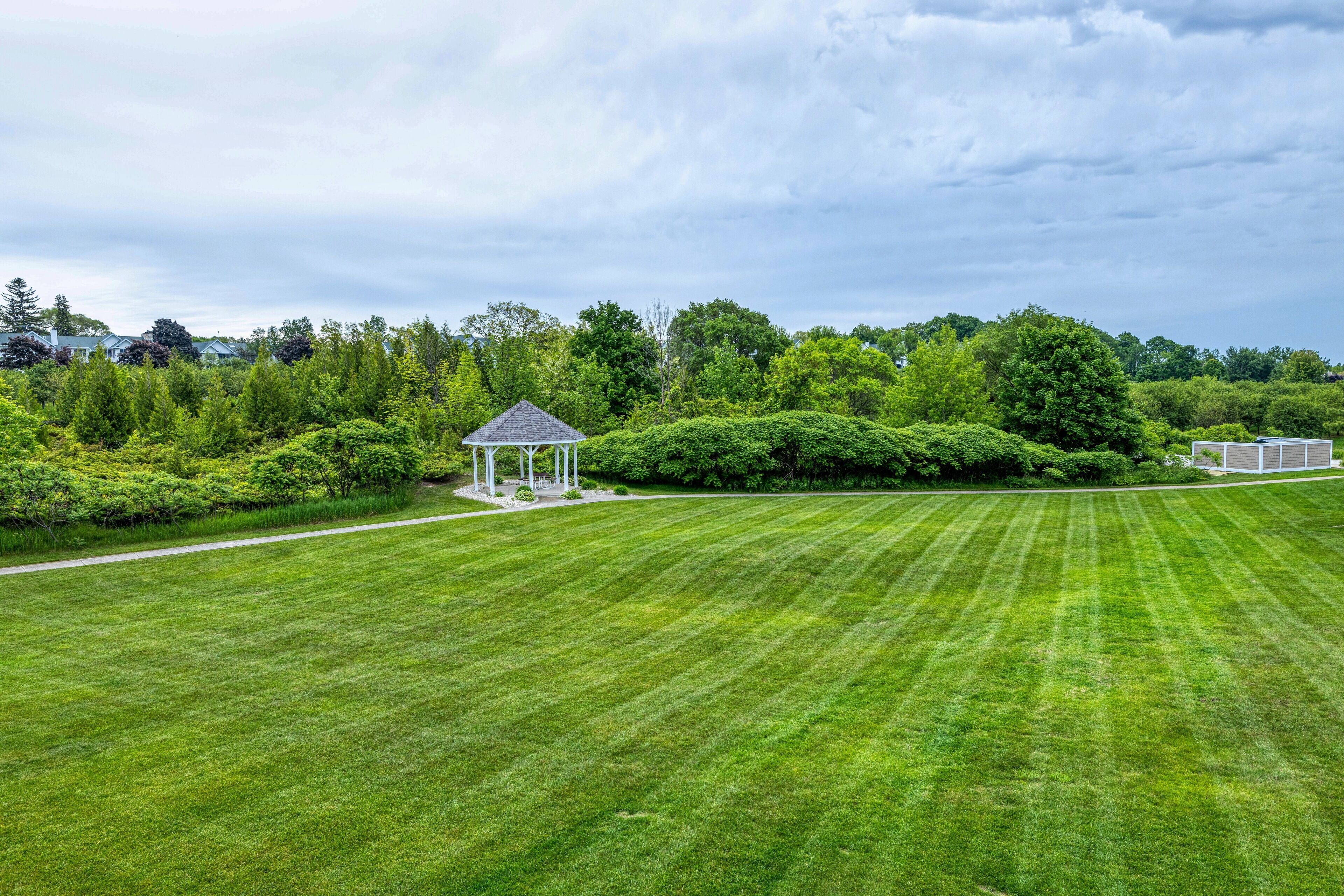 A well-maintained lawn with a gazebo and a small building, surrounded by dense greenery and trees.