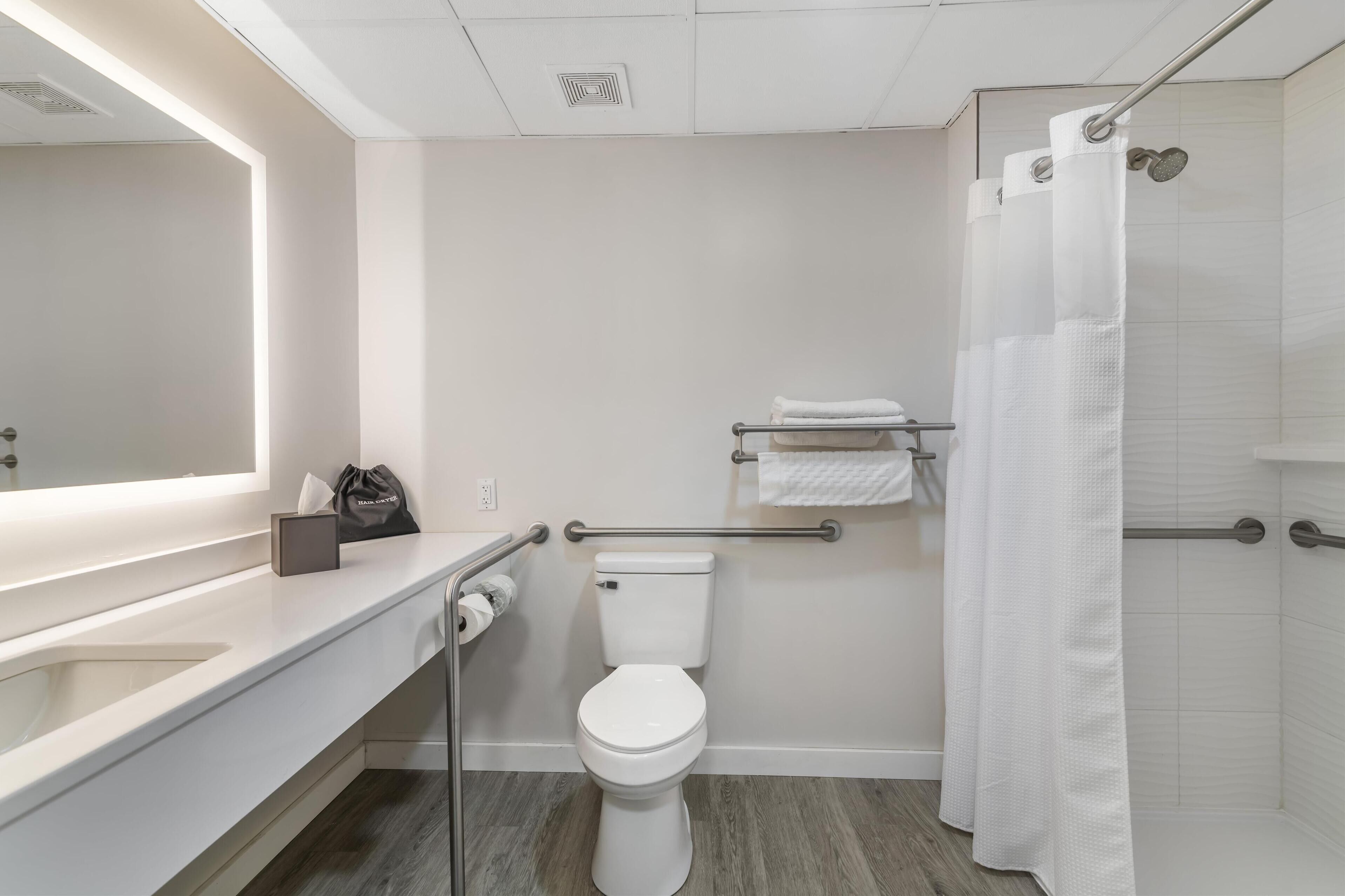 A modern bathroom with a white toilet, a sink with a mirror, a towel rack, and a shower with a curtain.