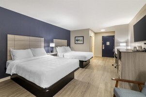 Habitación de hotel con dos camas, un escritorio, una silla, un televisor y una puerta que da a un baño.