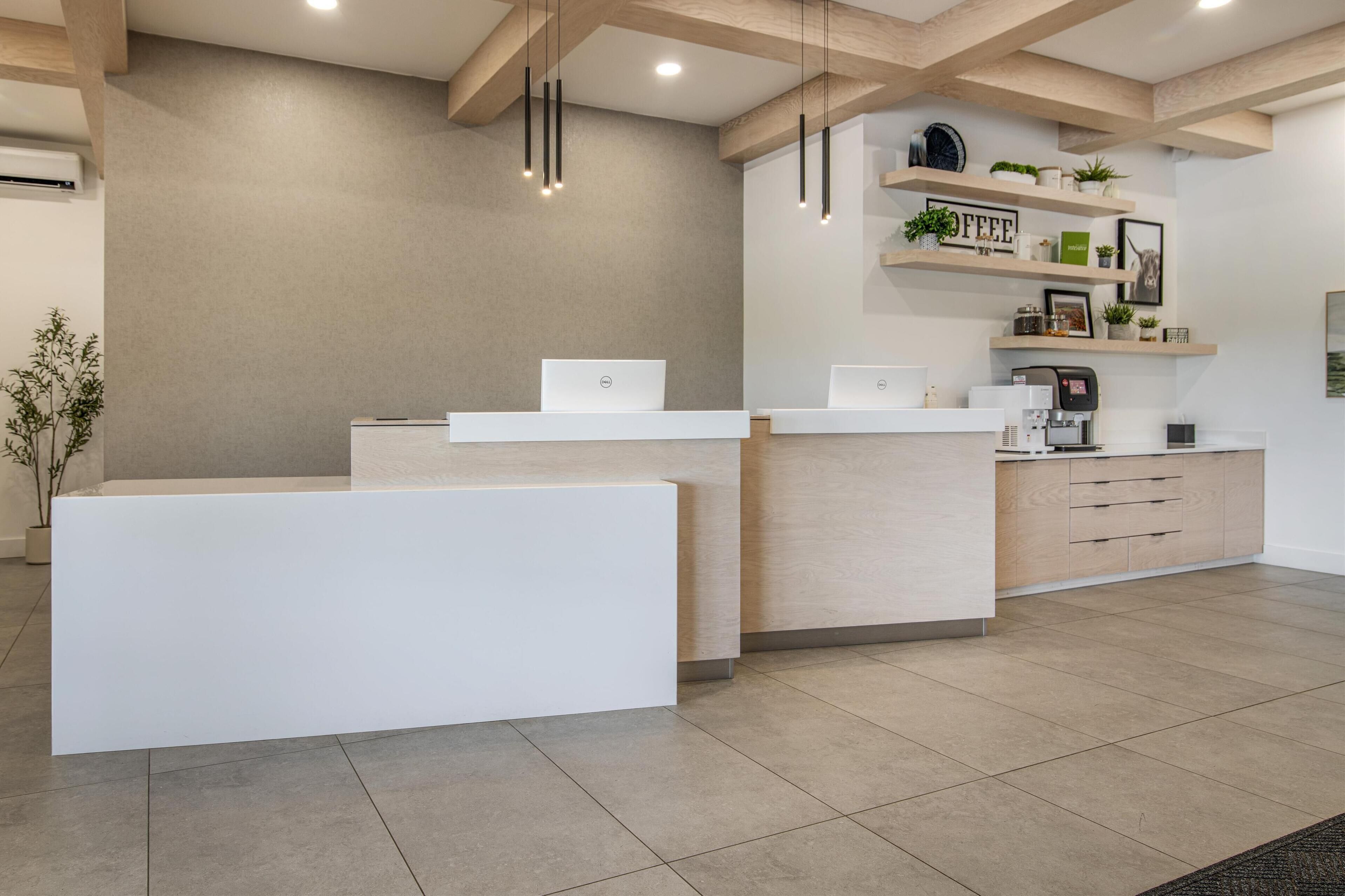 Un área de recepción de diseño moderno, con un mostrador de recepción, dos portátiles, una máquina de café y estanterías con plantas y decoración.