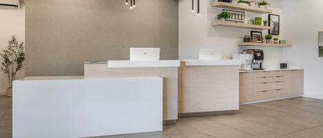 Un área de recepción de diseño moderno, con un mostrador de recepción, dos portátiles, una máquina de café y estanterías con plantas y decoración.