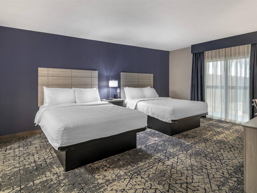 Une chambre d’hôtel avec deux lits, un bureau, une lampe et une grande fenêtre avec des rideaux.
