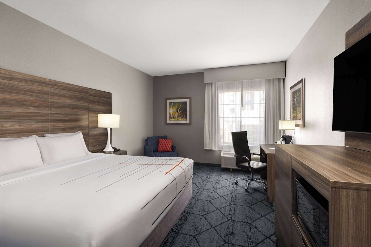 A hotel room with a large bed, a desk, a chair, a TV, and a window with curtains.