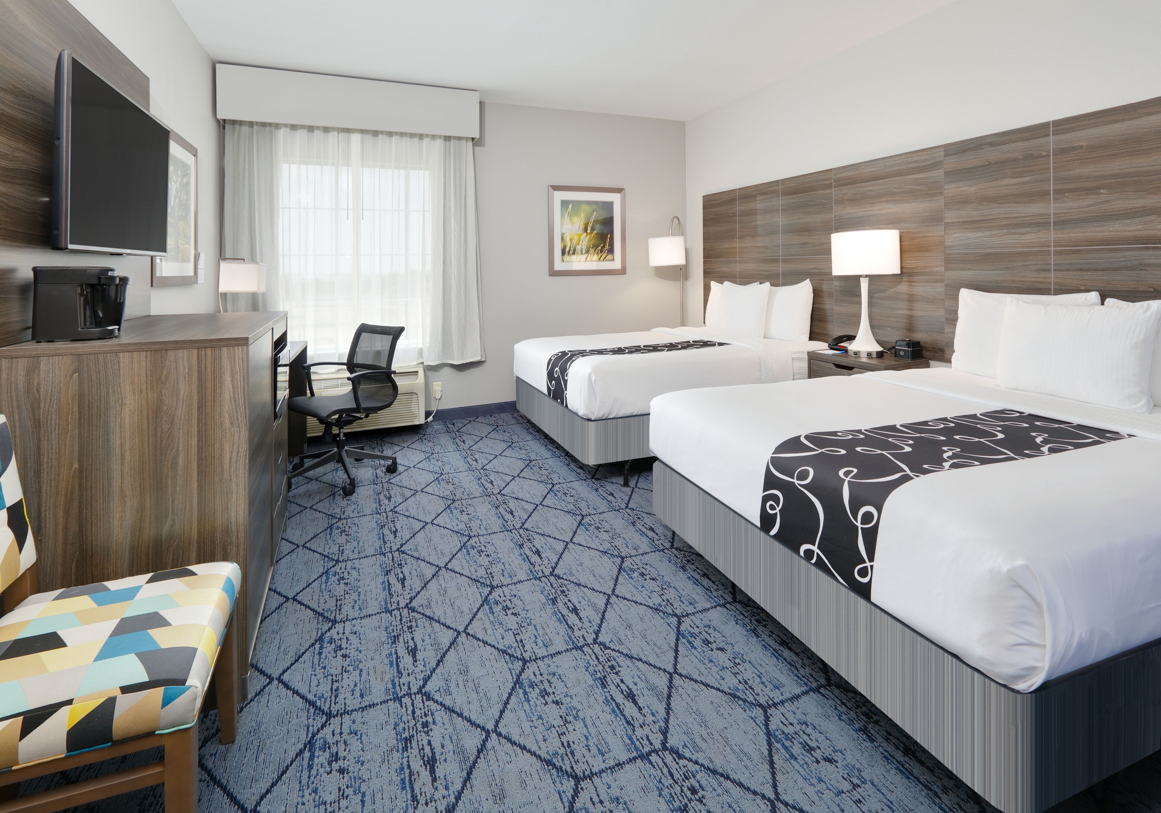 A hotel room with two beds, a desk with a computer, a chair, and a TV.
