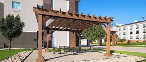 A covered outdoor seating area with a pergola, stone pathway, and benches.