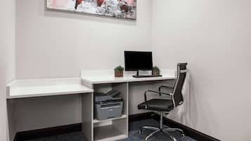 Um pequeno espaço de escritório com uma mesa branca, uma cadeira de escritório preta, uma impressora e um monitor de computador.
