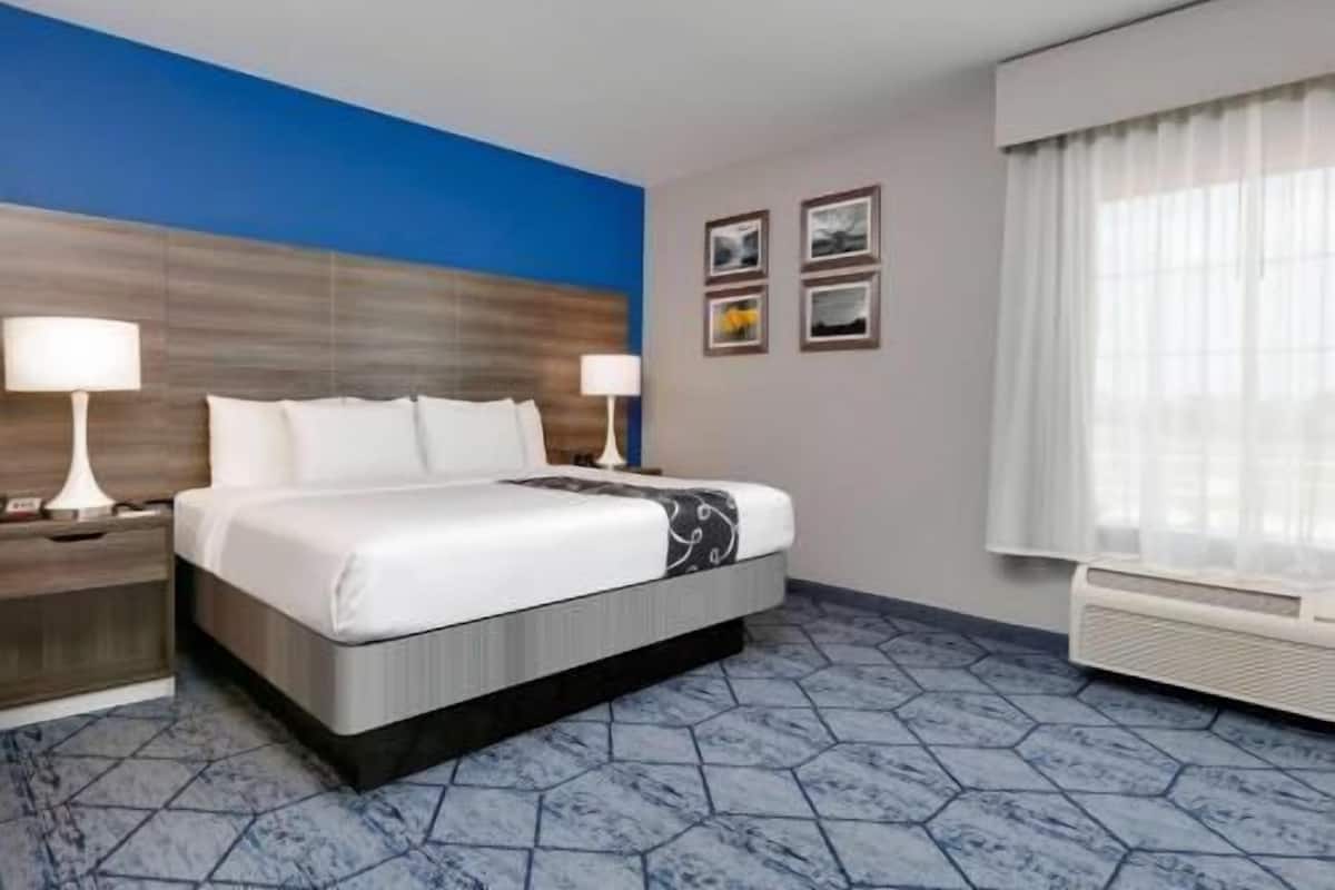 A hotel room with a bed, two bedside lamps, a window with curtains, and a wall with framed pictures.