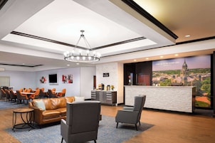 A hotel lobby with a reception desk, seating area, and a large window with a cityscape view.