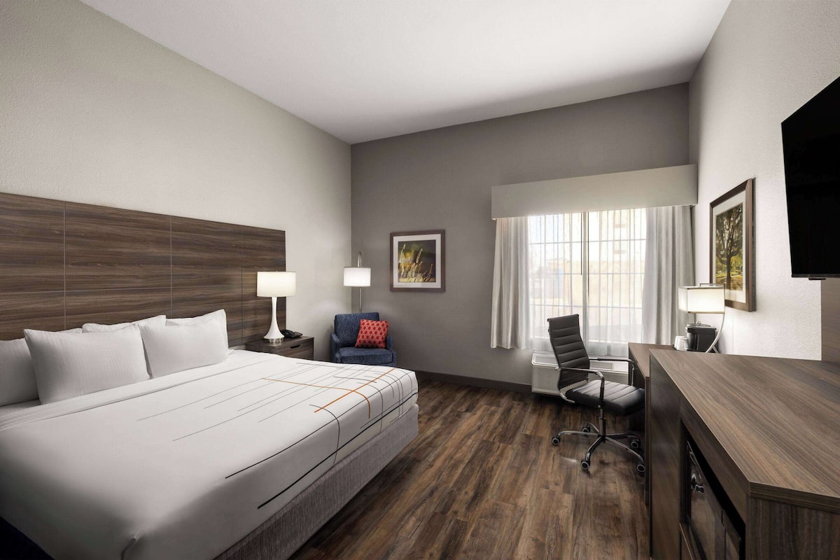 A hotel room with a large bed, a desk, a chair, and a window with curtains.