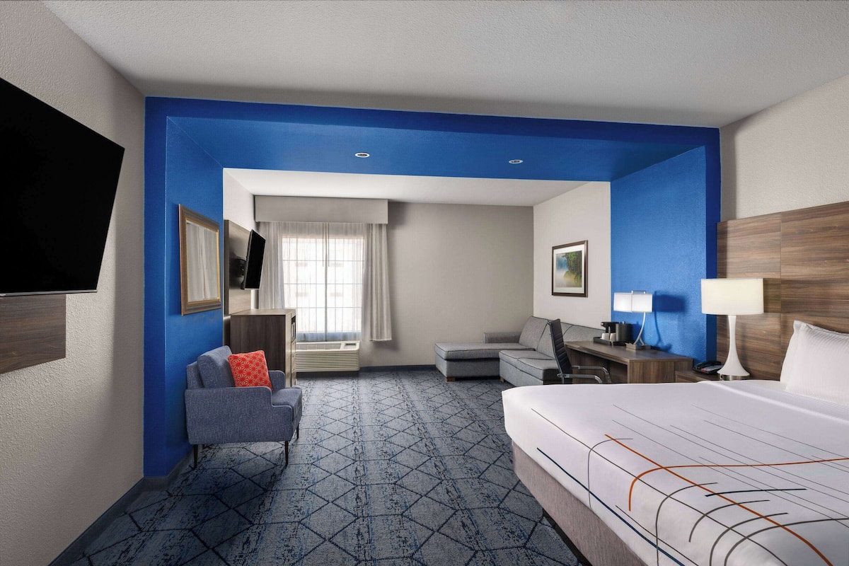 A hotel room with a bed, a desk, a chair, a TV, and a window with curtains.