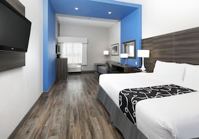 A hotel room with a large bed, a desk, a chair, a TV, and a bathroom visible through an open door.
