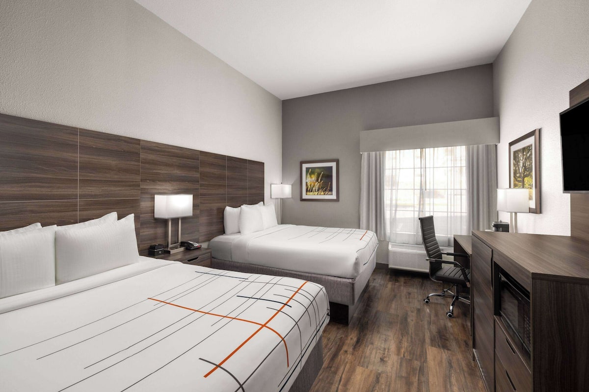A hotel room with two beds, a desk, a chair, a TV, and a window with curtains.