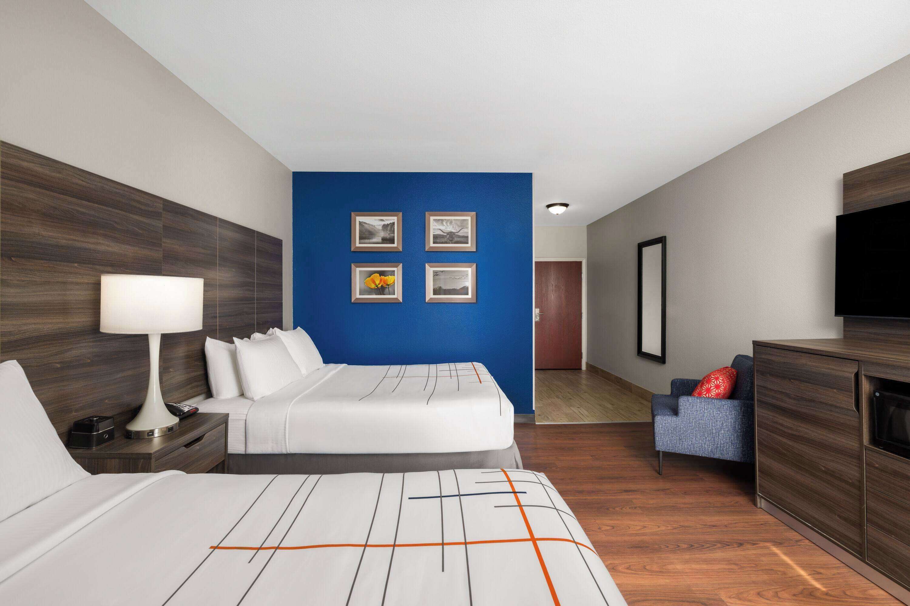 A modern hotel room with a large bed, a desk, a chair, a TV, and a blue accent wall.