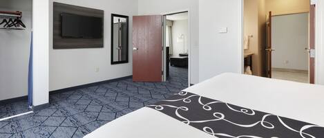 A hotel room with a bed, a television mounted on the wall, a wardrobe, and a bathroom visible through an open door.