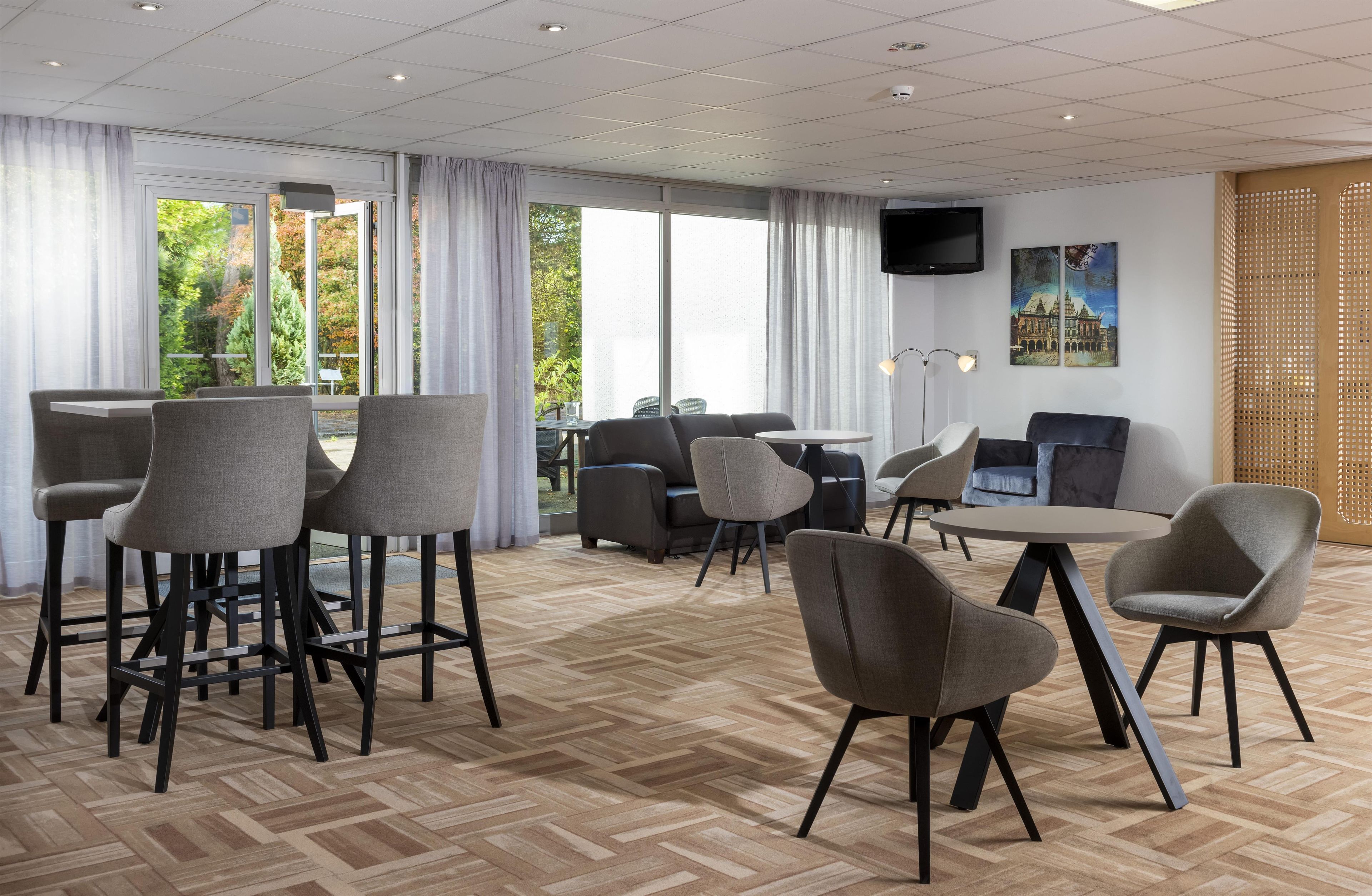 Habitación de hotel con zona de comedor, asientos y televisor en la pared.