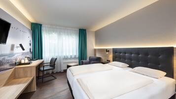 Una habitación de hotel con cama, escritorio, silla y televisor en la pared.