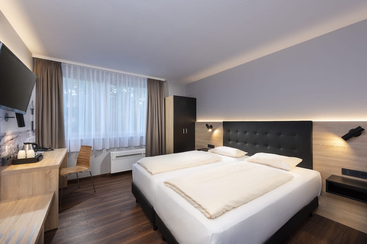 A hotel room with a bed, a desk, a chair, a TV, and a window with curtains.