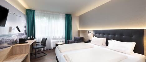 Una habitación de hotel con cama, escritorio, silla y televisor en la pared.