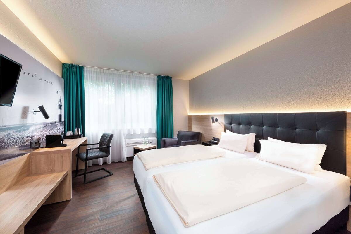 A hotel room with a large bed, a desk with a chair, a TV, and a window with curtains.
