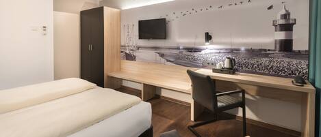 Habitación de hotel con cama, escritorio, silla, televisión y un mural en la pared.