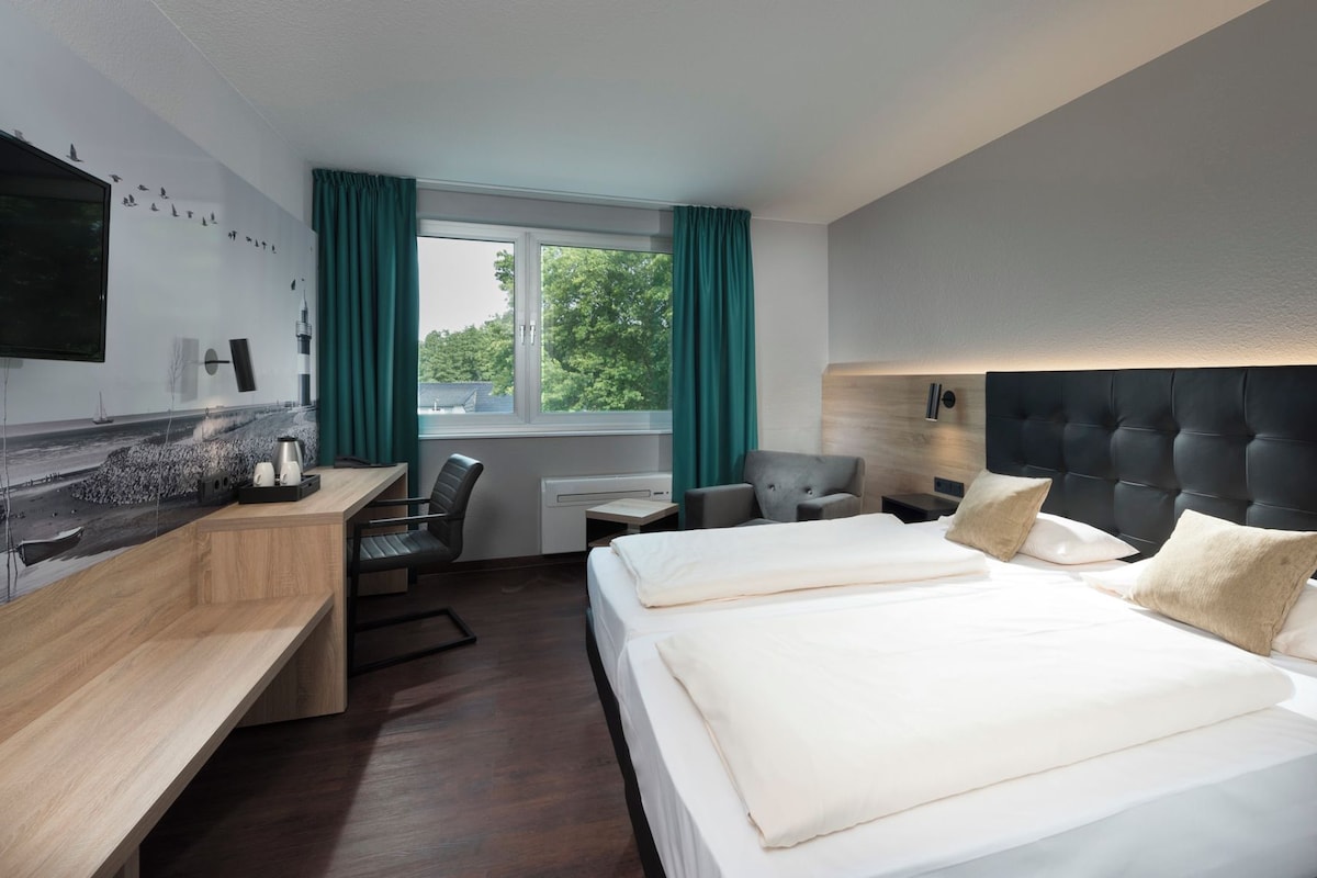 Une chambre d’hôtel avec un lit, un bureau, une chaise, une télévision et une fenêtre avec des rideaux.