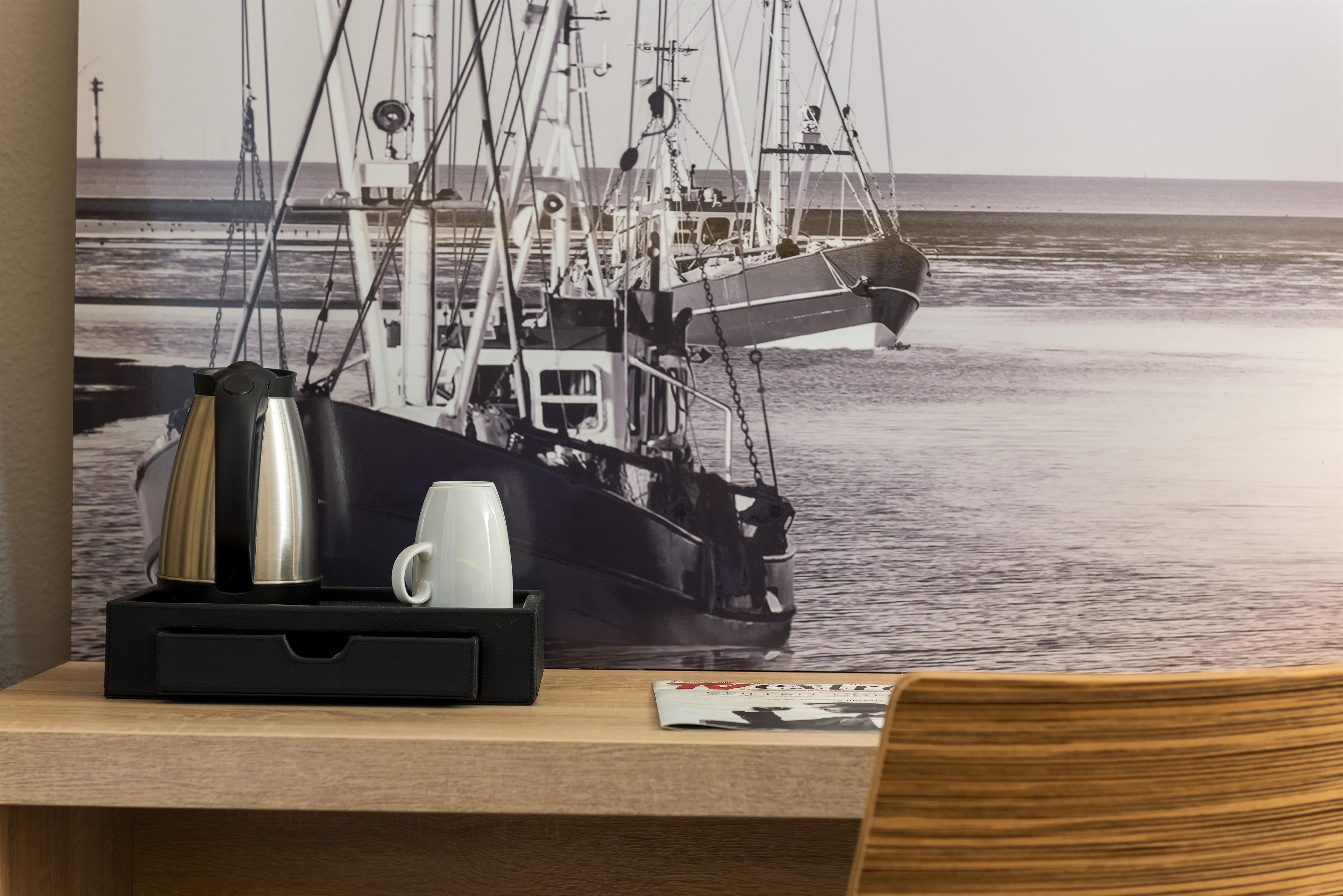 A desk with a coffee maker, mug, and a magazine, with a poster of a ship on the wall.
