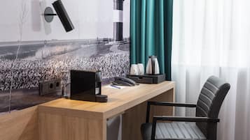 Ein Hotelzimmer mit einem Holztisch, einem schwarzen Bürostuhl, einer Wandlampe, einem Telefon und einer Kaffeemaschine.