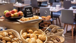 Un bufé de desayuno con panes, bollería y frutas variadas.