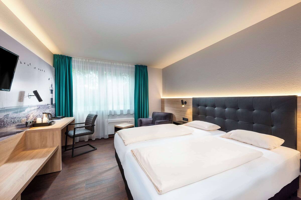 A hotel room with a large bed, a desk, a chair, a TV, and a window with curtains.