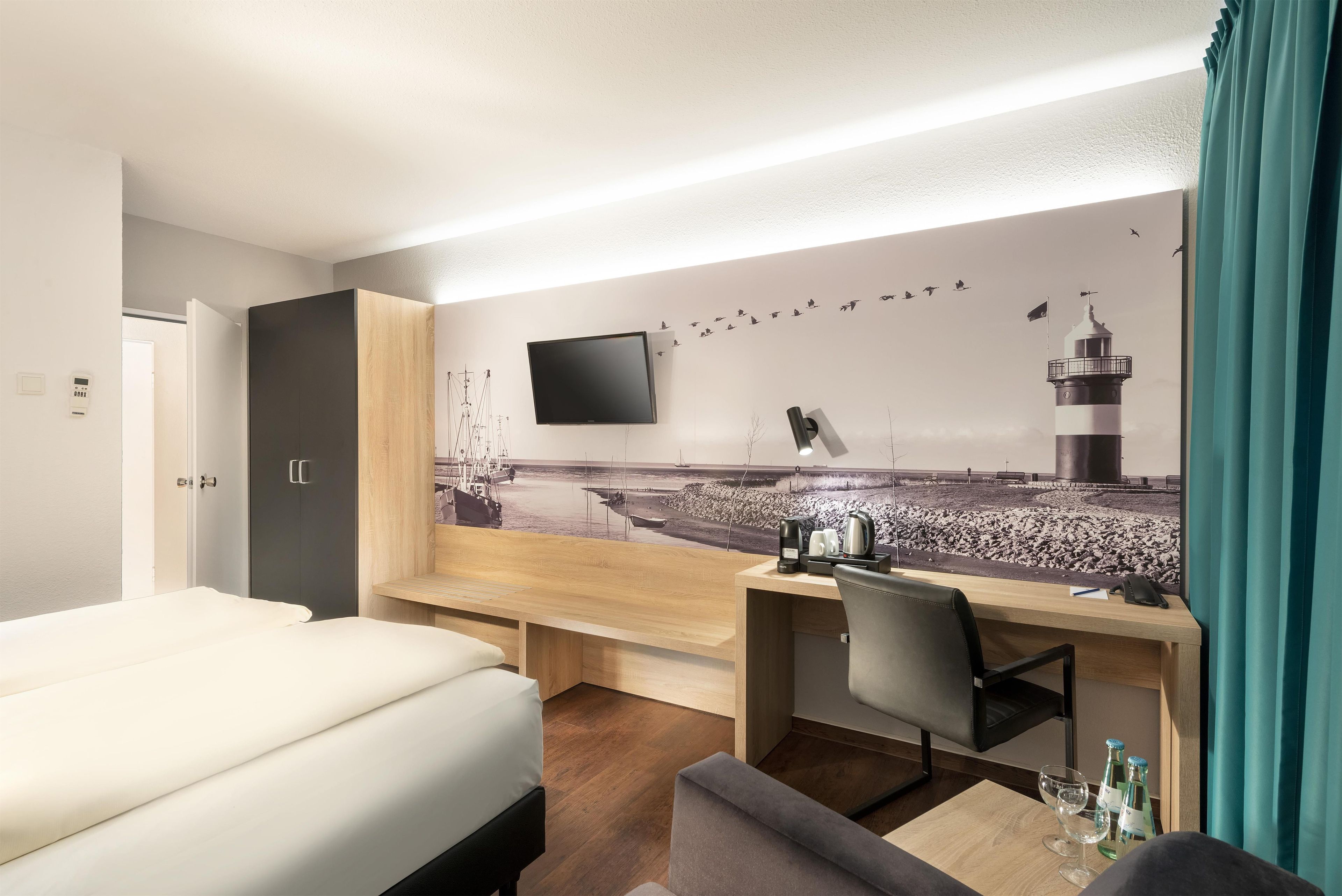 A hotel room with a bed, a desk, a chair, a flat-screen TV, and a wall mural of a beach scene.